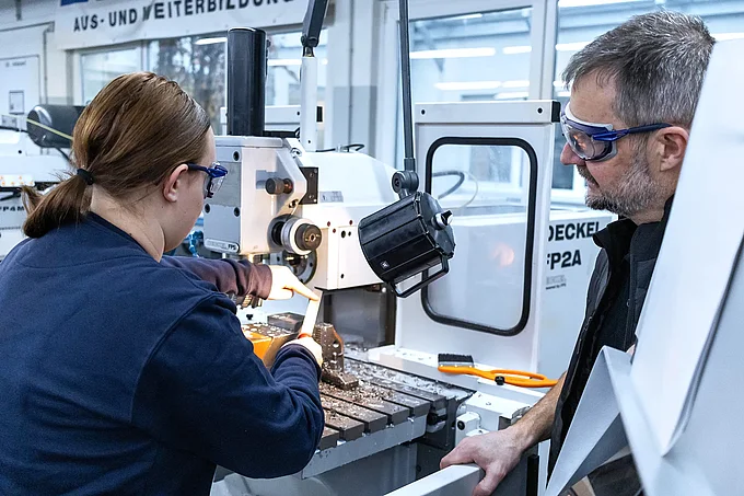 Ausbilder erklärt angehender Fertigungsmechanikerin etwas an einer Fräsmaschine